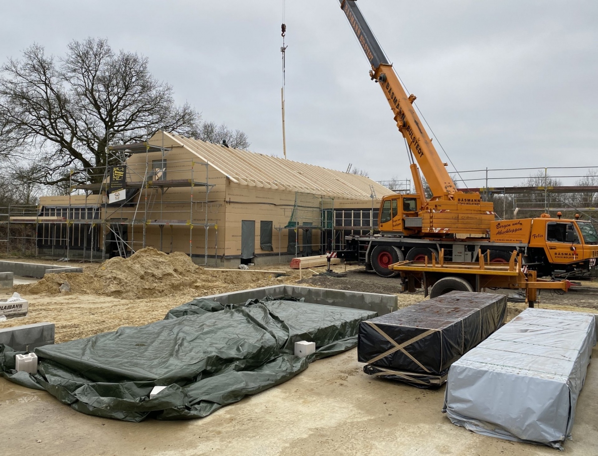 Ein Kran steht neben dem Rohbau eines Hauses aus Holz.