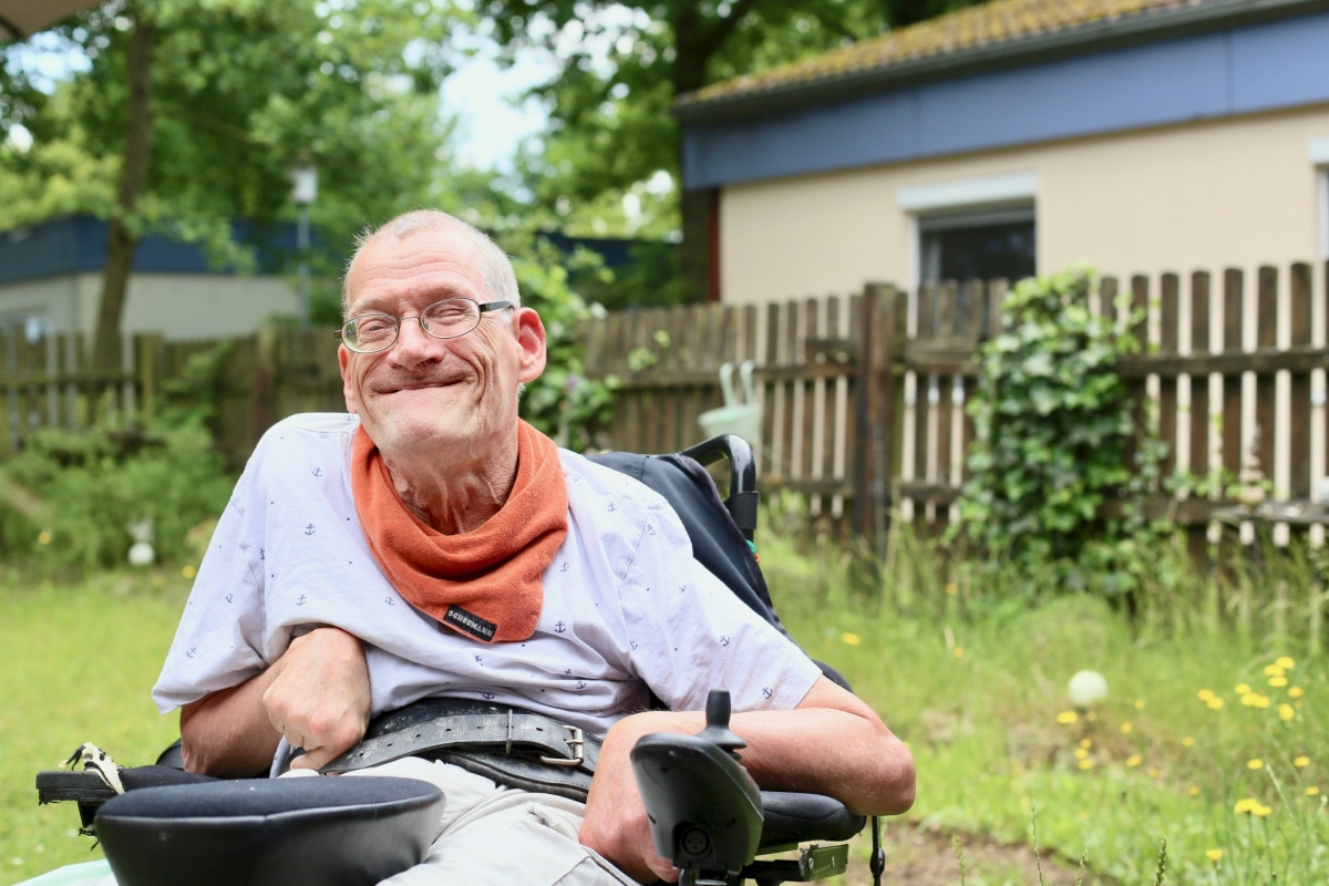 Ein Mann sitzt in einem Rollstuhl im Garten und lacht.