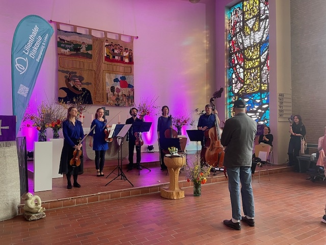 In einer Kirche stehen fünf Musiker mit Streichinstrumenten vor dem Alter, ein Mann schaut sich das an. 